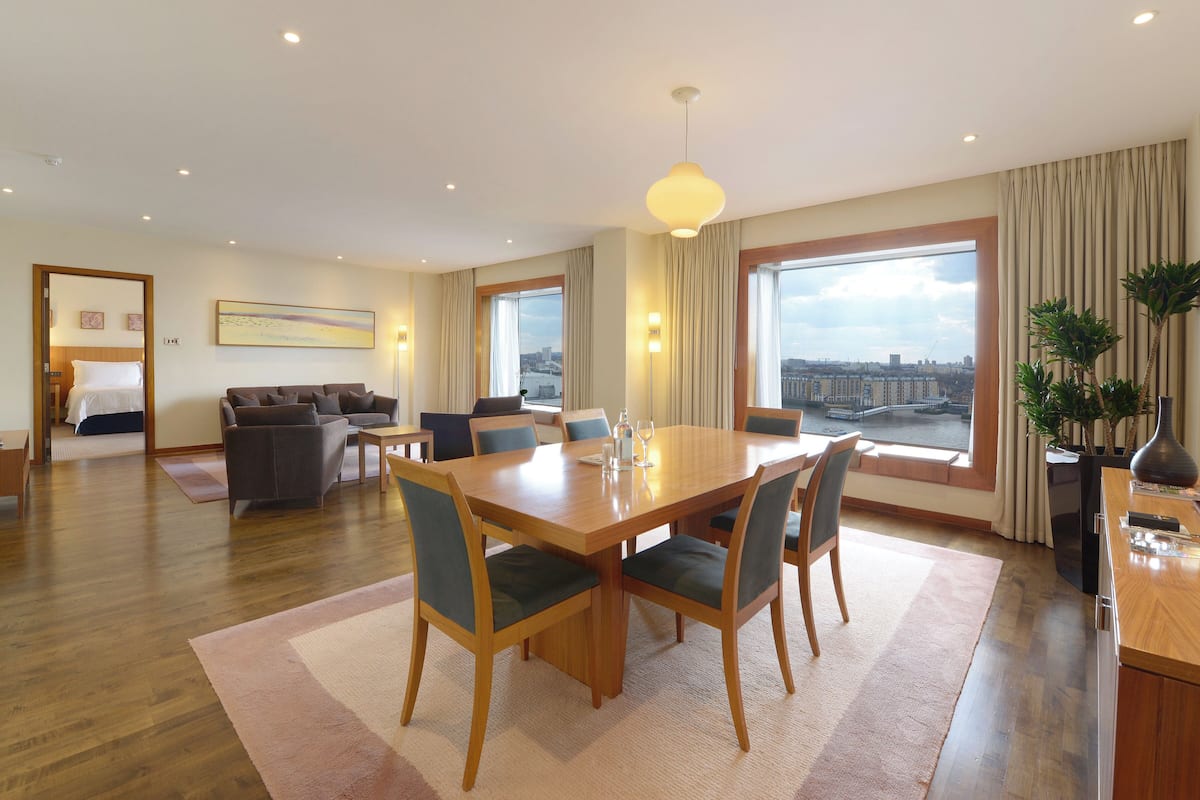 A spacious living area with a dining table, sofas, and a large window offering a city view.