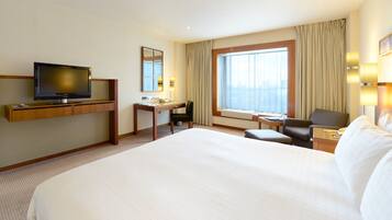 A hotel room with a large bed, a desk with a chair, a television, and a window with curtains.