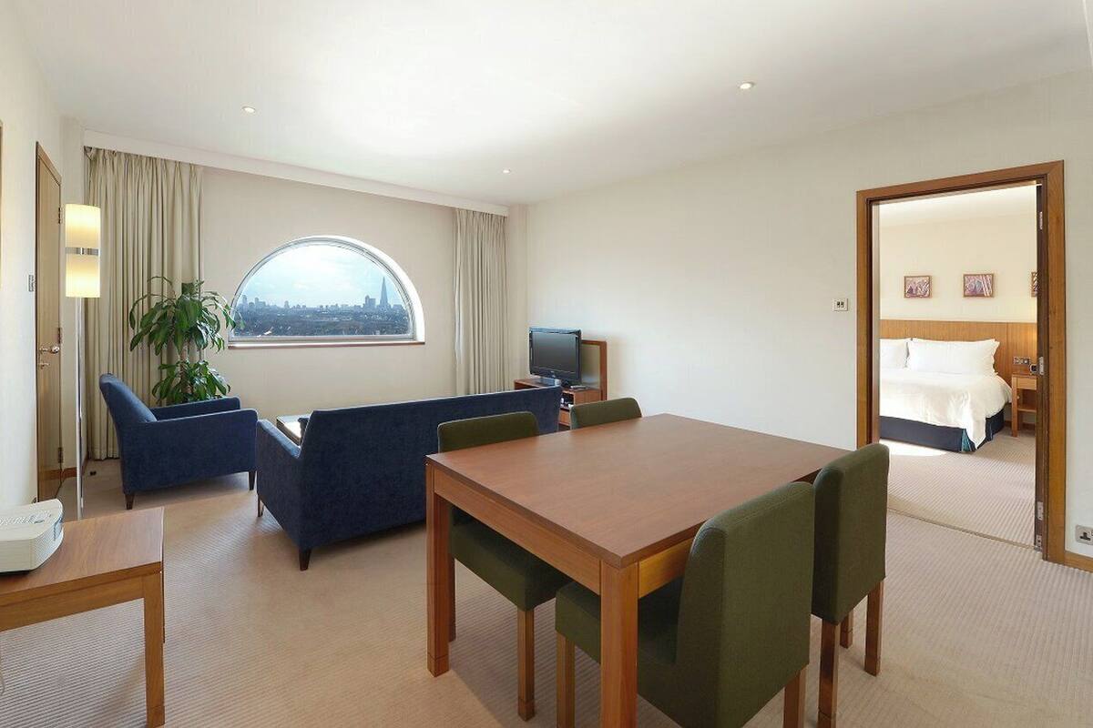 A hotel room with a sofa, a dining table, a TV, and a bed.