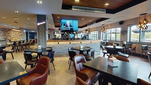 A modern restaurant with wooden ceiling, large windows, and a television screen displaying a news program. - Village Hotel Nottingham (Nottingham)