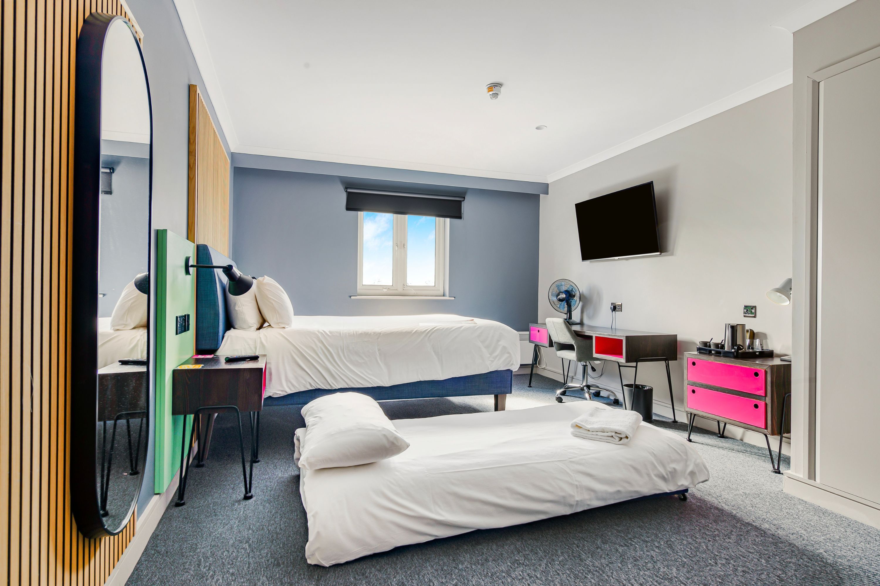 A modern hotel room with a large bed, a desk, a chair, a TV, and a window.