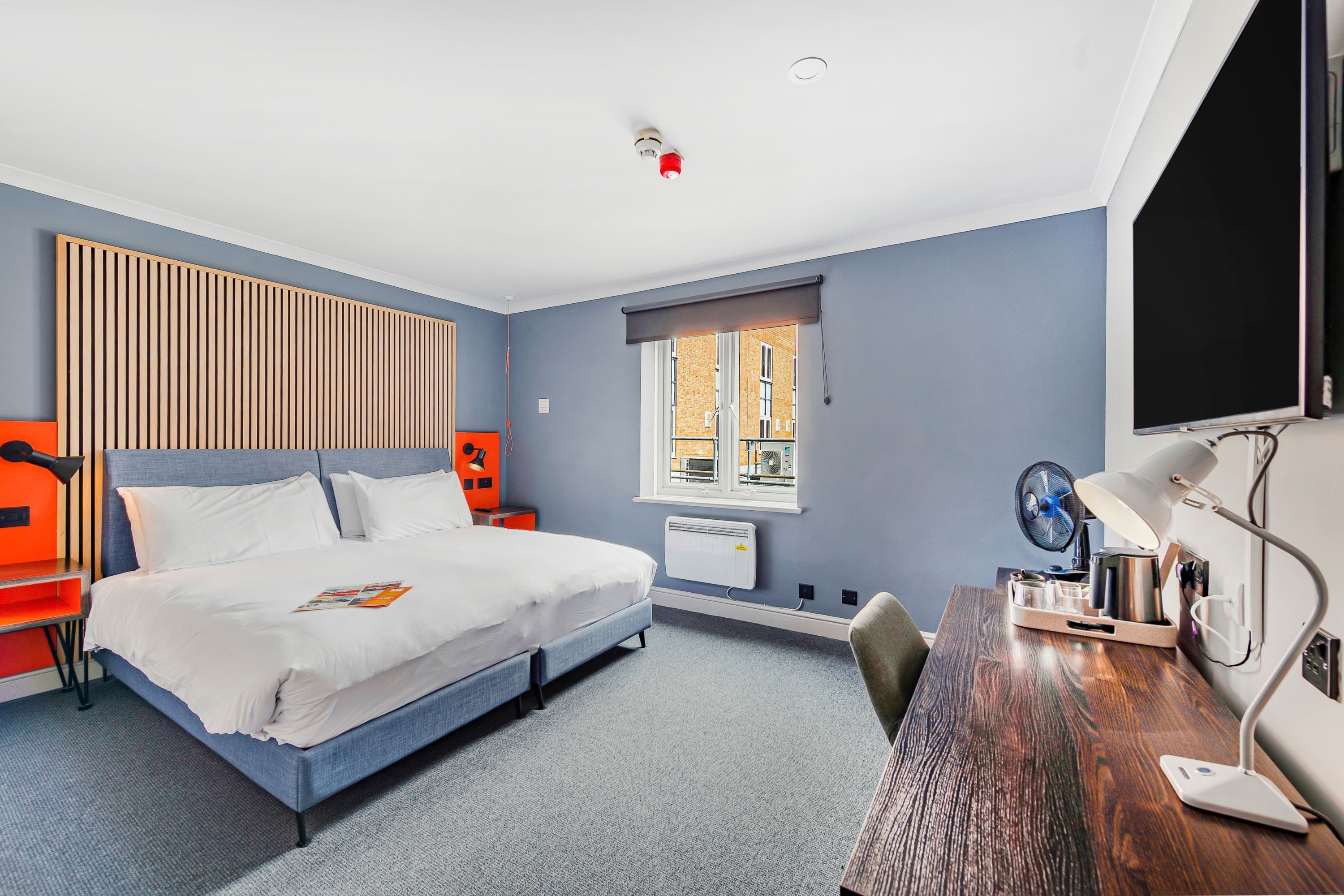 Une chambre d’hôtel moderne, équipée d’un lit, d’un bureau et d’une fenêtre.