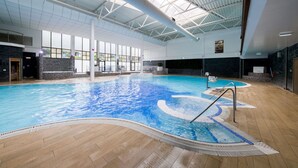An indoor swimming pool with a tiled floor, a diving board, and a large windowed wall. - Village Hotel Nottingham (Nottingham)