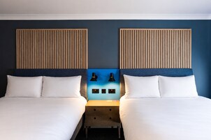 Habitación doble con dos camas, una mesita de noche, dos lámparas de pared y una pared de acento azul.