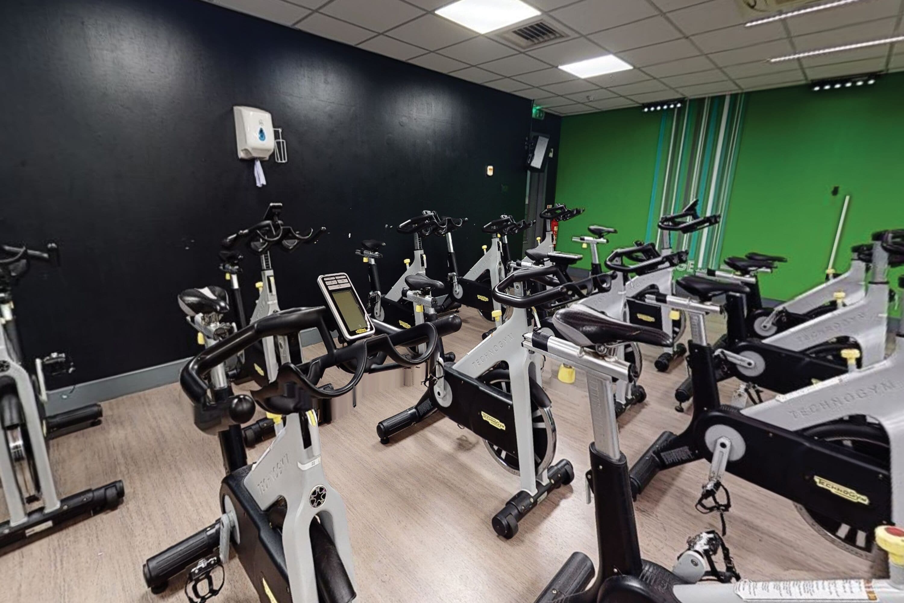 Una palestra con diverse cyclette e macchinari cardio, un muro verde e un soffitto bianco.