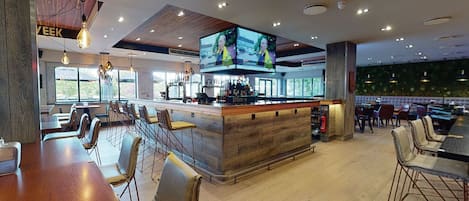A modern bar area with a wooden bar counter, multiple seating options including bar stools and tables, and large flat-screen TVs mounted on the ceiling.