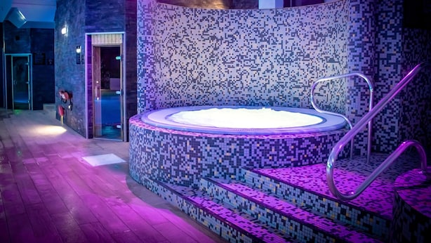 A hot tub with mosaic tile walls and steps, surrounded by a wooden deck. - Village Hotel Nottingham (Nottingham)