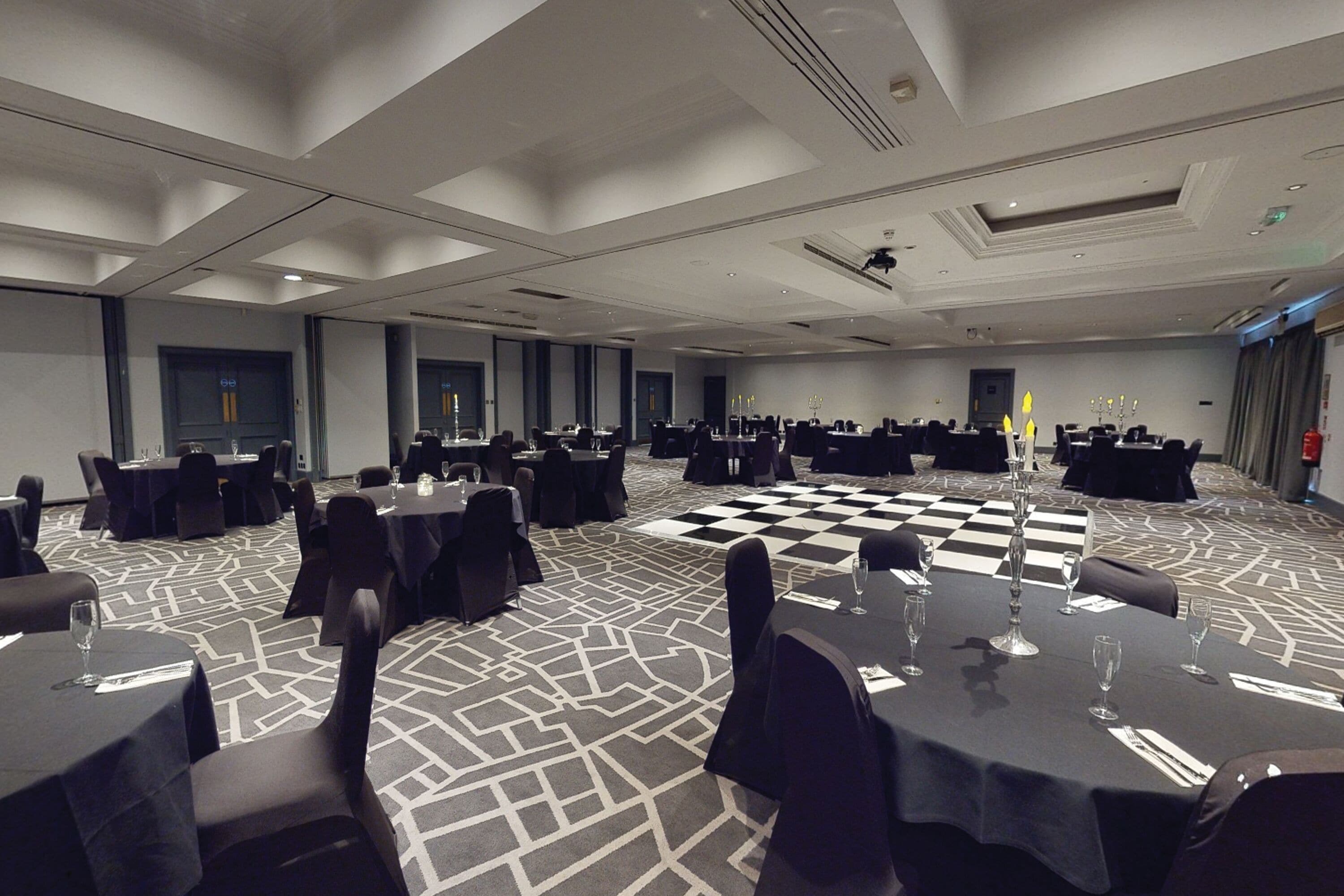 A conference room with multiple tables and chairs, a checkered floor, and a modern ceiling design.