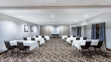 A conference room with a large table, chairs, a projector screen, and a patterned carpet.