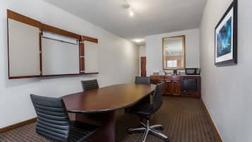Una sala de conferencias con una mesa grande, cuatro sillas, un área de cocina con un refrigerador y un espejo en la pared.