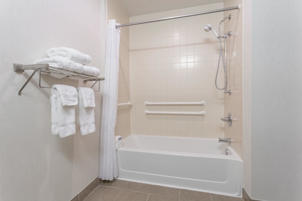 Un baño moderno con una bañera, una ducha con cabezal de ducha de mano y un perchero con toallas dobladas.