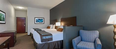A hotel room with a bed, a desk, a chair, a lamp, and a picture on the wall.