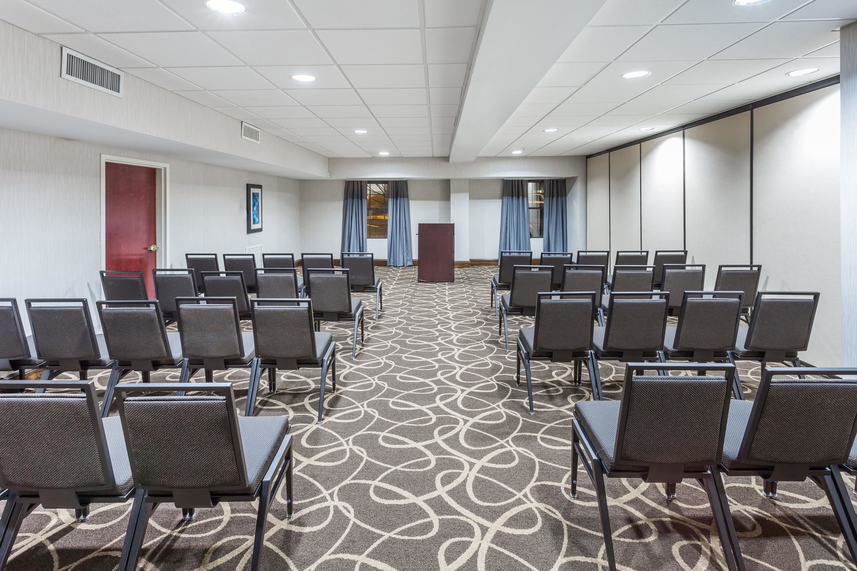 A conference room with rows of chairs, a podium, and a patterned carpet.
