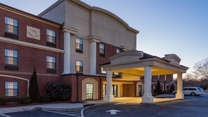 A multi-story hotel with a brick facade, a covered entrance, and a parking lot. - Wingate by Wyndham High Point/Greensboro/Airport South (High Point)