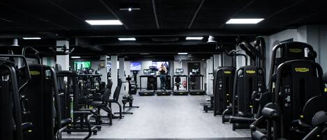 A gym with various exercise machines, a television screen, and a person working out.