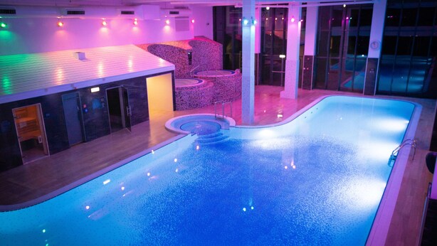 An indoor swimming pool with a tiled deck, a seating area with chairs, and a poolside bar. - Village Hotel Wirral (Wirral)