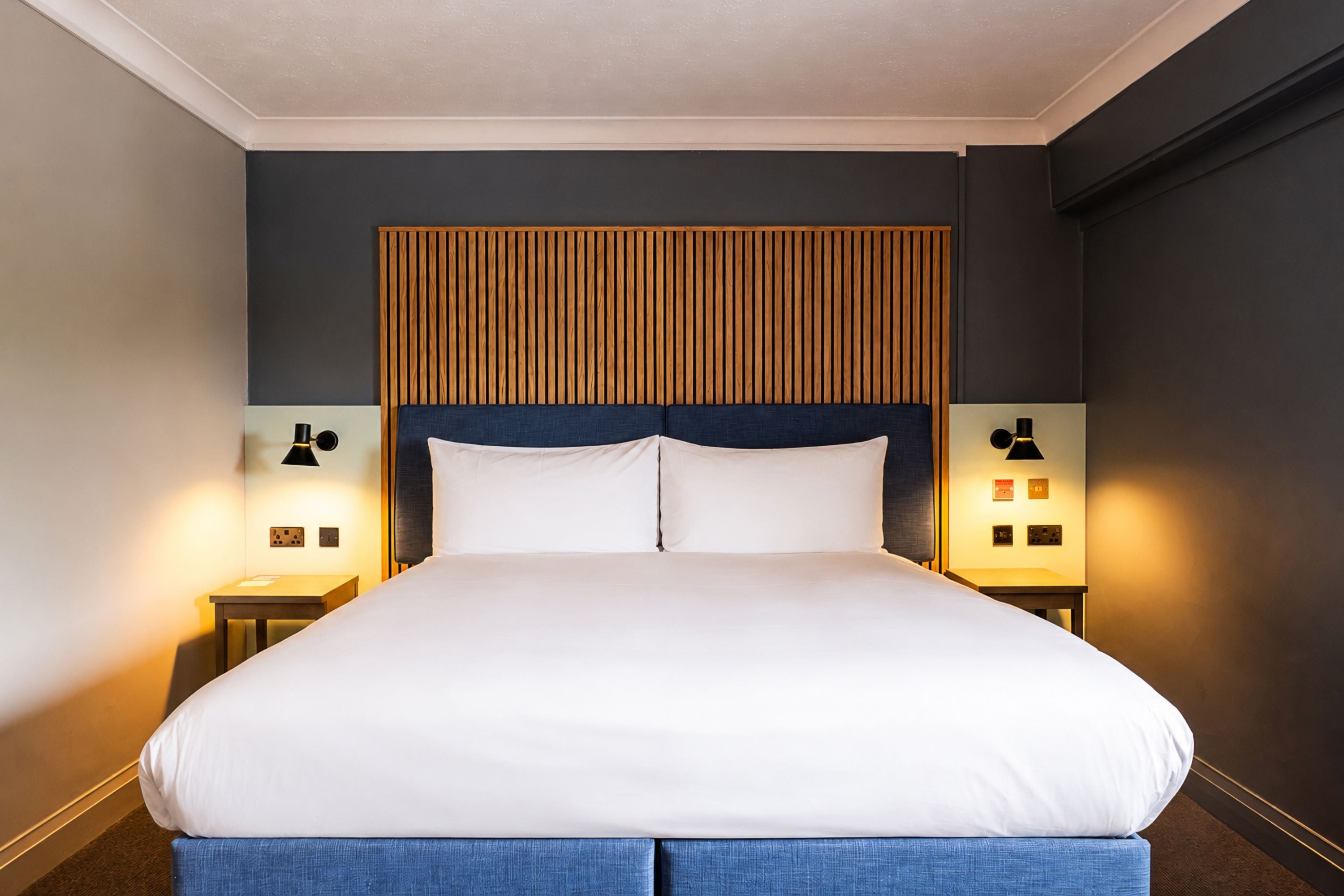 A hotel room with a large bed, two bedside tables, and a wall-mounted headboard.
