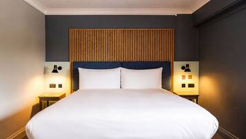 A hotel room with a large bed, two bedside tables, and a wall-mounted headboard.