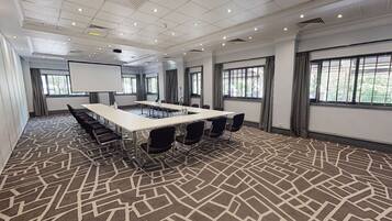 A conference room with a long table, chairs, a projector screen, and large windows.