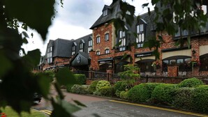 A traditional brick building with a pub and kitchen sign, surrounded by well-maintained hedges and a paved street. - Village Hotel Wirral (Wirral)