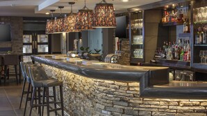 Un espace bar doté d’un comptoir en pierre, de tabourets de bar et d’une variété de bouteilles et de verres.