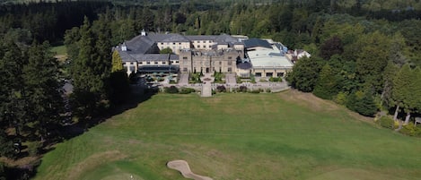 Vista aérea de una extensa propiedad con un amplio césped, un campo de golf y un edificio imponente con múltiples ventanas y una entrada central.