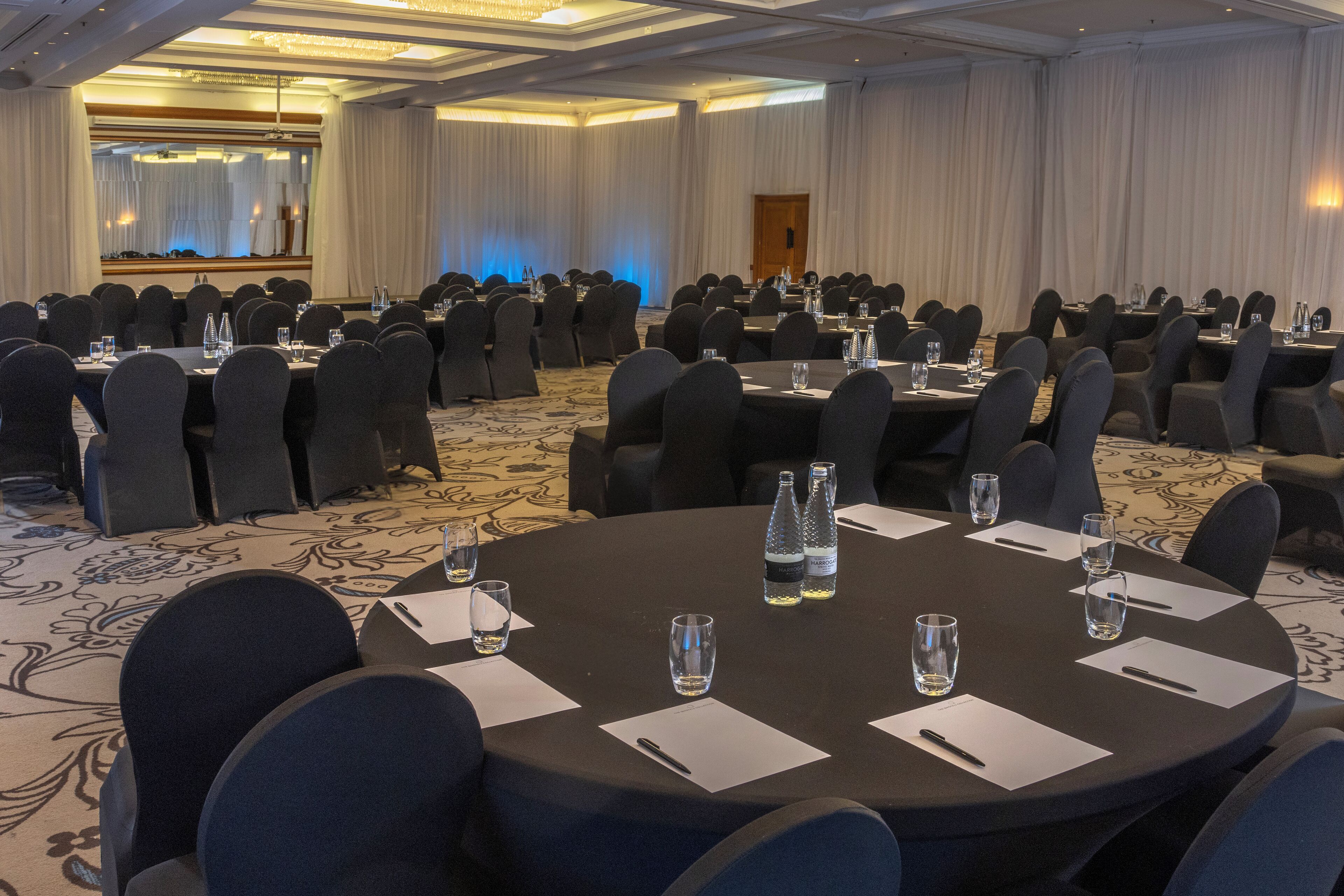 Une salle de conférence équipée de tables rondes, de chaises et de bouteilles d’eau.