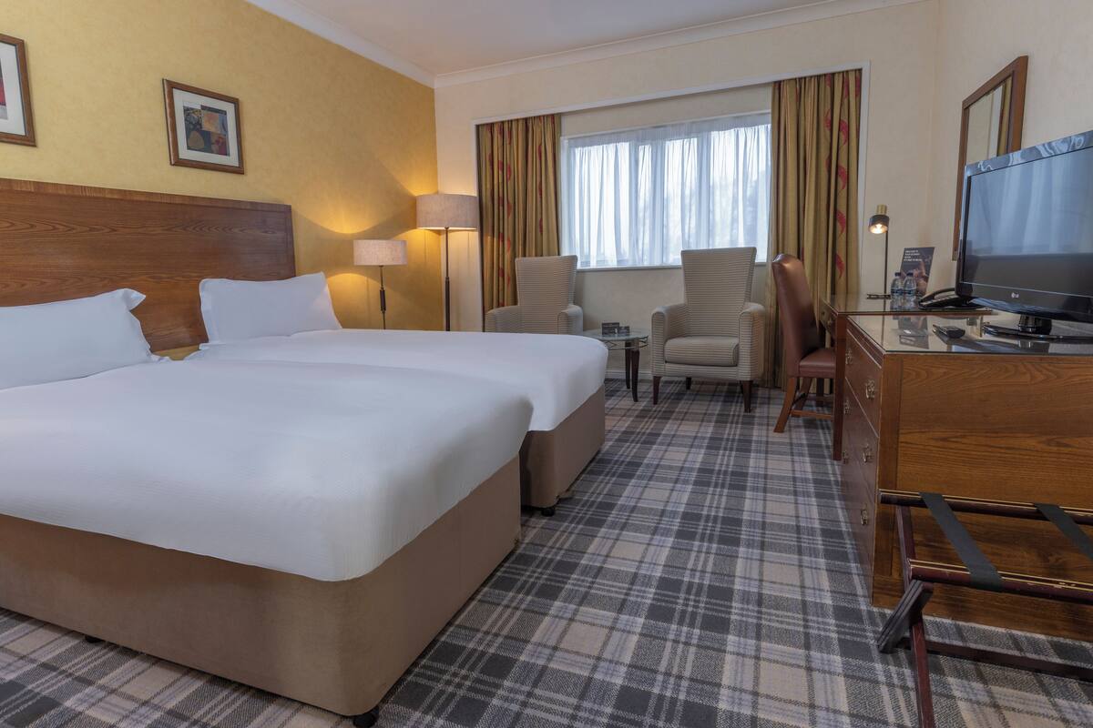 A hotel room with a large bed, two armchairs, a desk with a television, and a small table.