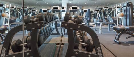 Un gimnasio con diversos equipos de ejercicio, incluyendo cintas de correr, máquinas de pesas y pesas libres.