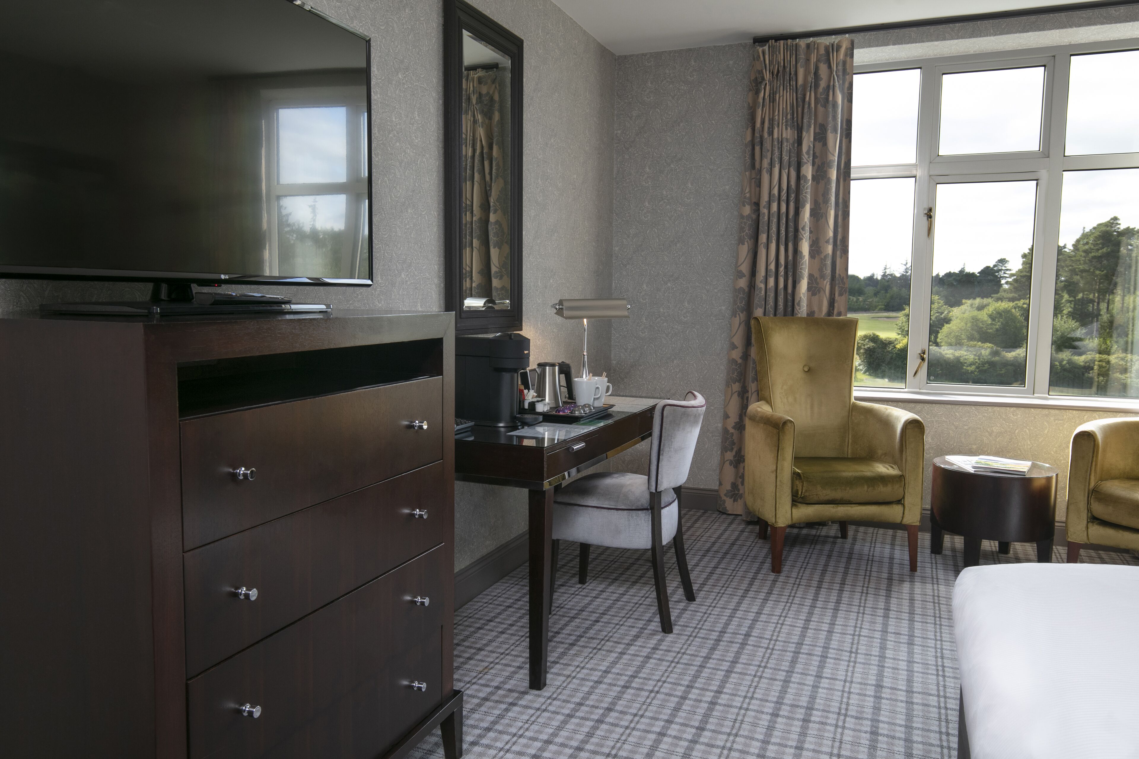 Habitación de hotel con televisor de pantalla plana, escritorio con lámpara, dos sillones y una cama.