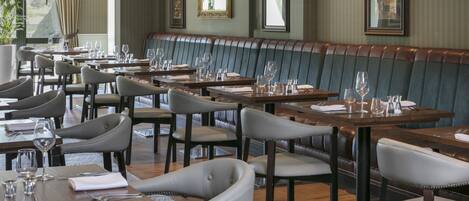 Un restaurante con una larga banqueta, varias mesas con sillas y cuadros en las paredes.