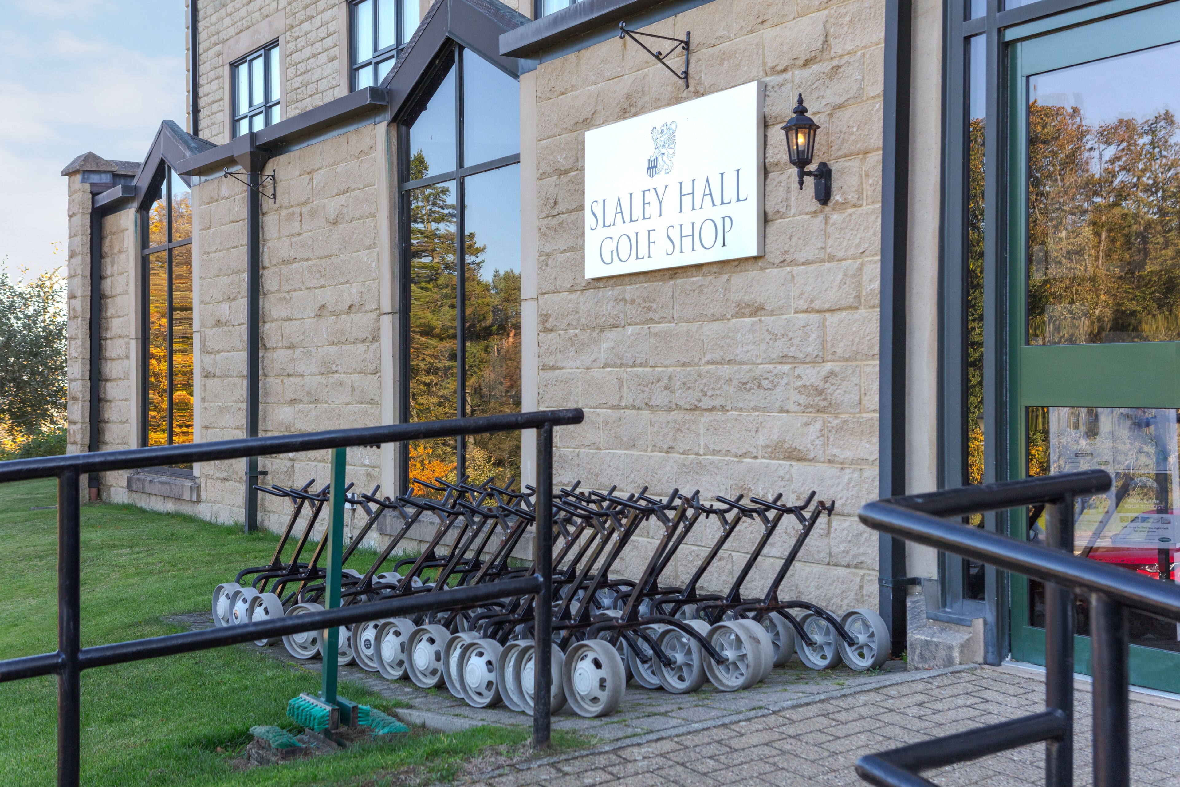 Un edificio de piedra con un cartel que dice "Slaley Hall Golf Shop" y una fila de carritos de golf afuera.