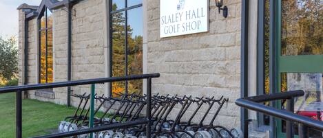 Un bâtiment en pierre avec une enseigne indiquant « Magasin de golf de Slaley Hall » et une rangée de voiturettes de golf à l’extérieur.