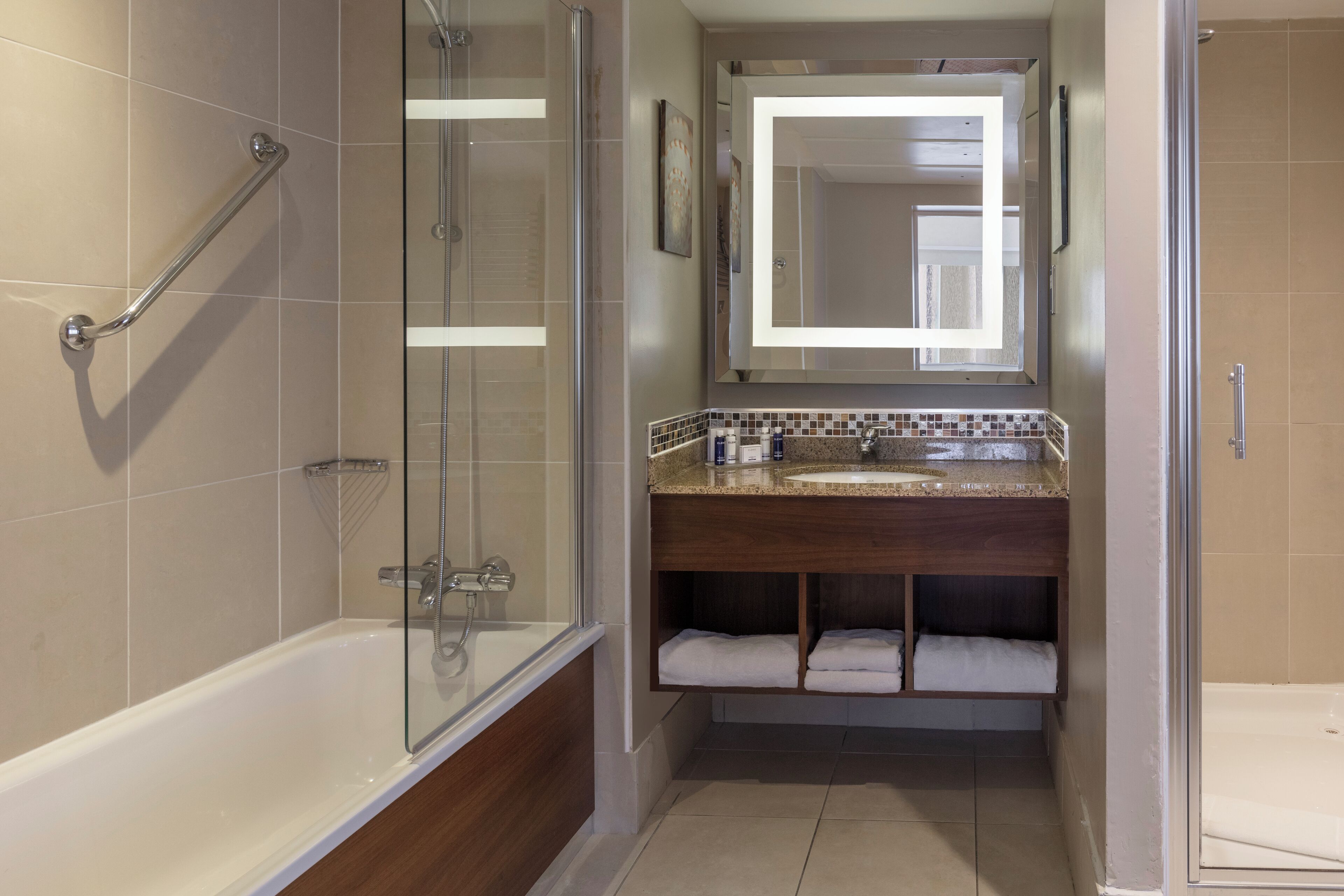 A bathroom with a glass-enclosed shower, a bathtub, a vanity with a mirror, and a towel rack.