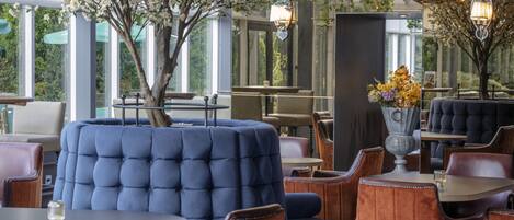 A restaurant with blue upholstered seating, wooden tables, and a large tree with white blossoms.