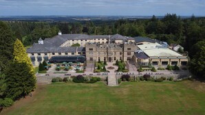 Un grand hôtel à plusieurs étages, doté d’une cour intérieure, entouré d’une végétation luxuriante et offrant une vue panoramique sur la campagne.