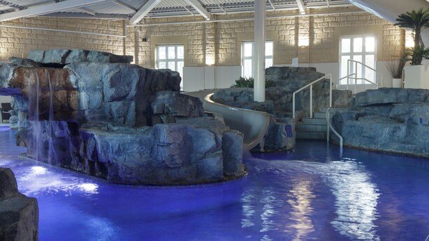 Une piscine intérieure agrémentée d’une cascade, entourée de formations rocheuses et d’un escalier.