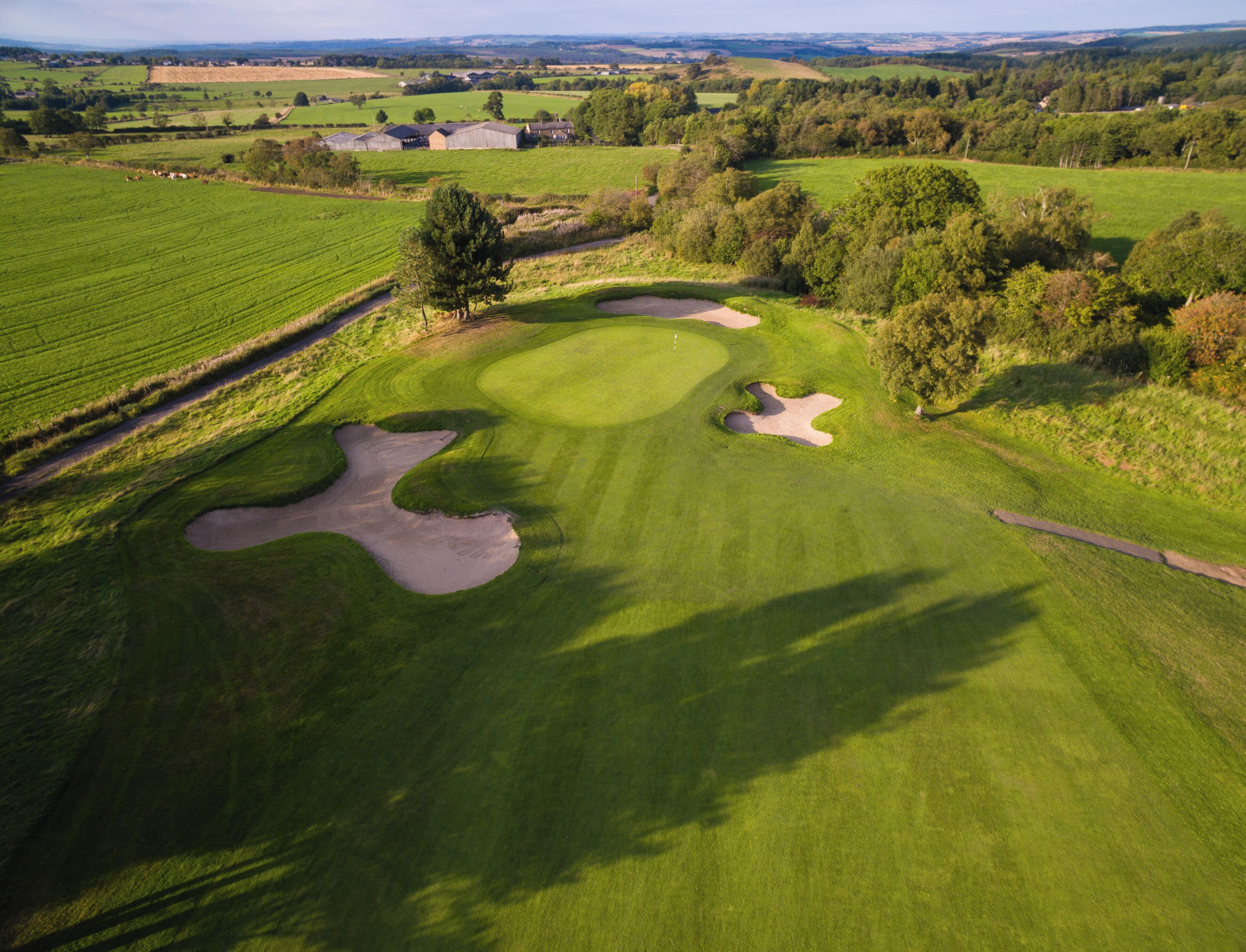 An aerial view of a golf course with sand bunkers, a pond, and surrounding fields.