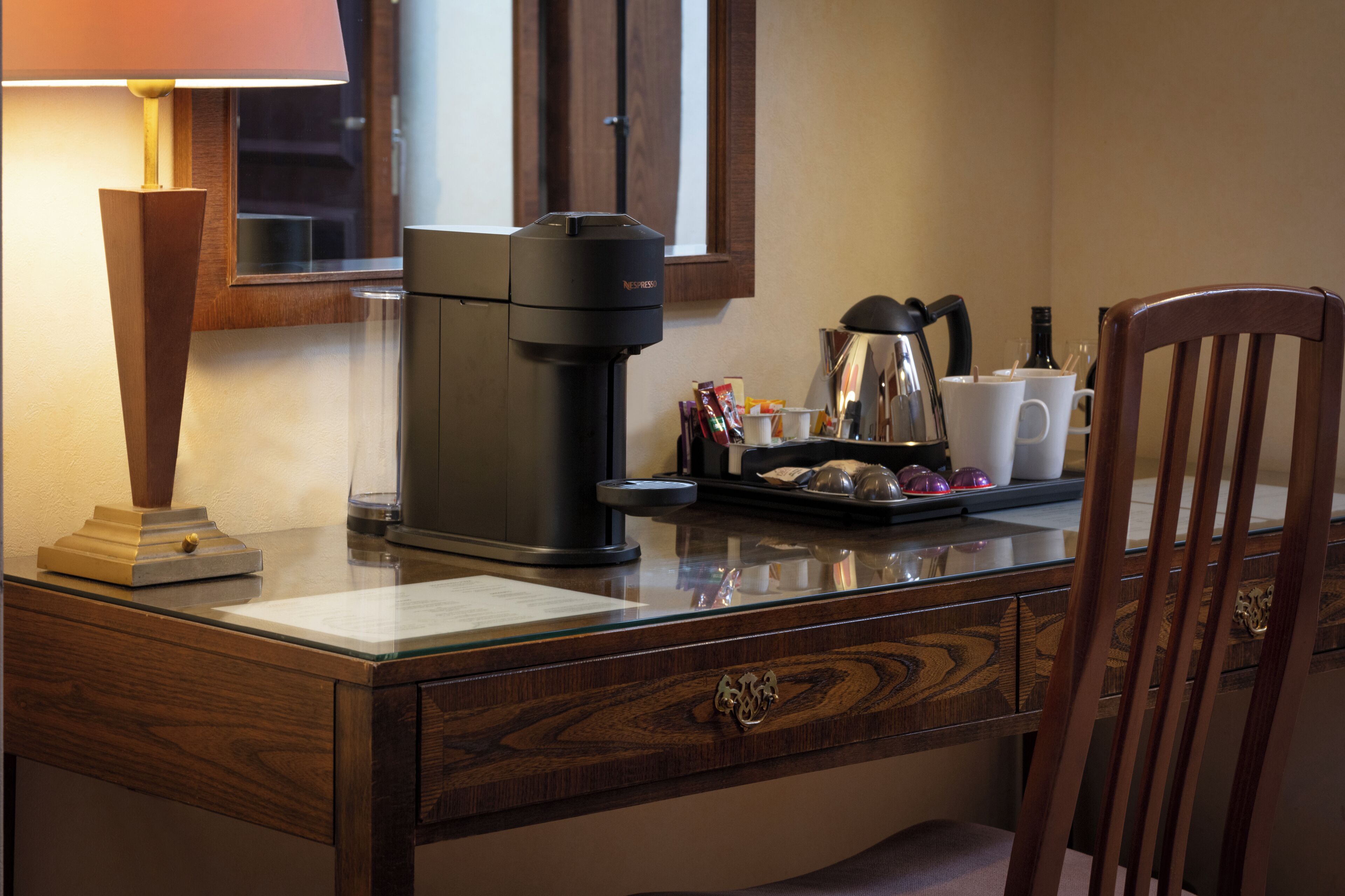 A wooden desk with a coffee maker, a lamp, and a cup of coffee.