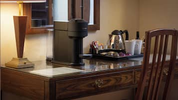 A wooden desk with a coffee maker, a lamp, and a cup of coffee.