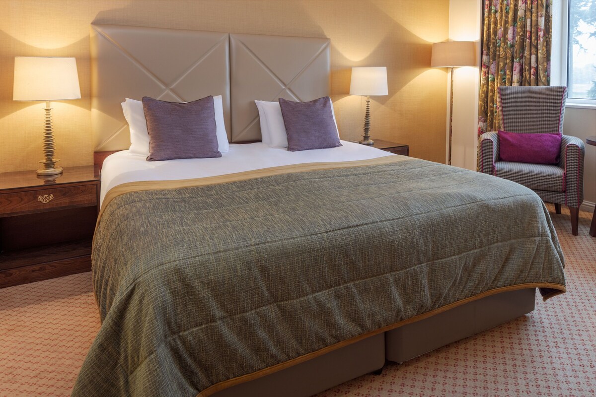 A hotel room with a large bed, two bedside tables with lamps, a chair, and a window with curtains.