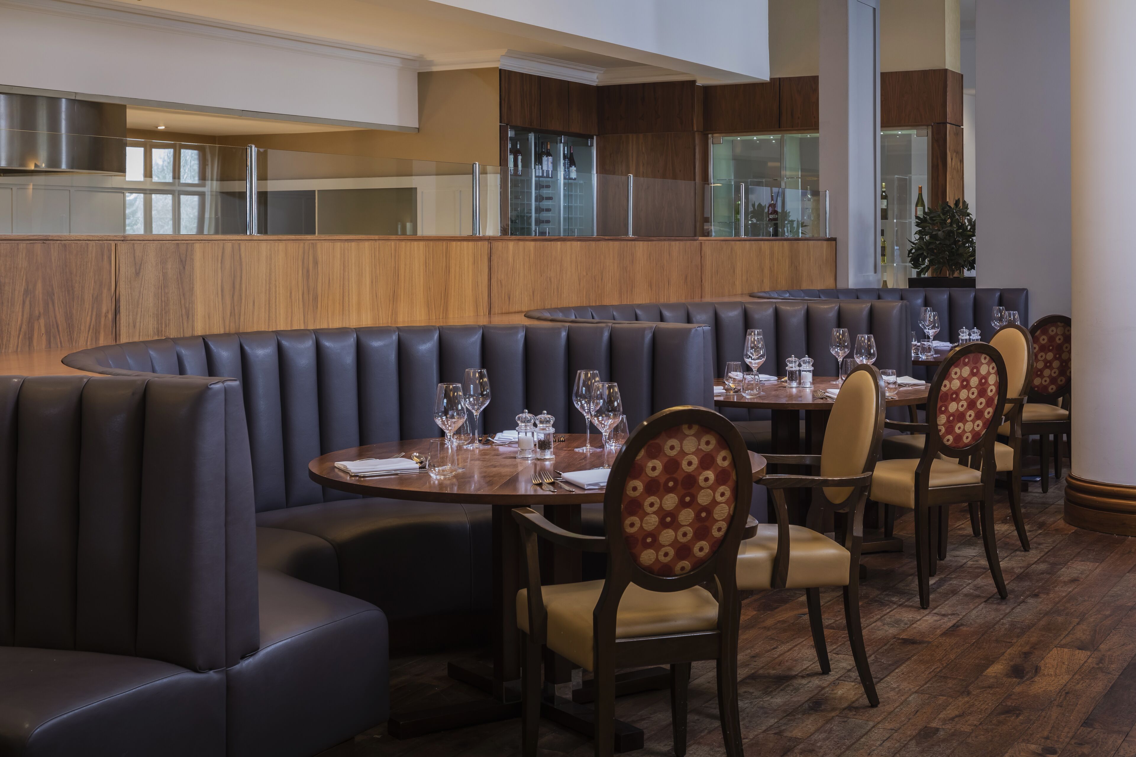 Un restaurante con asientos tipo cabina y mesas redondas, con una decoración moderna y detalles de madera, además de una planta grande.