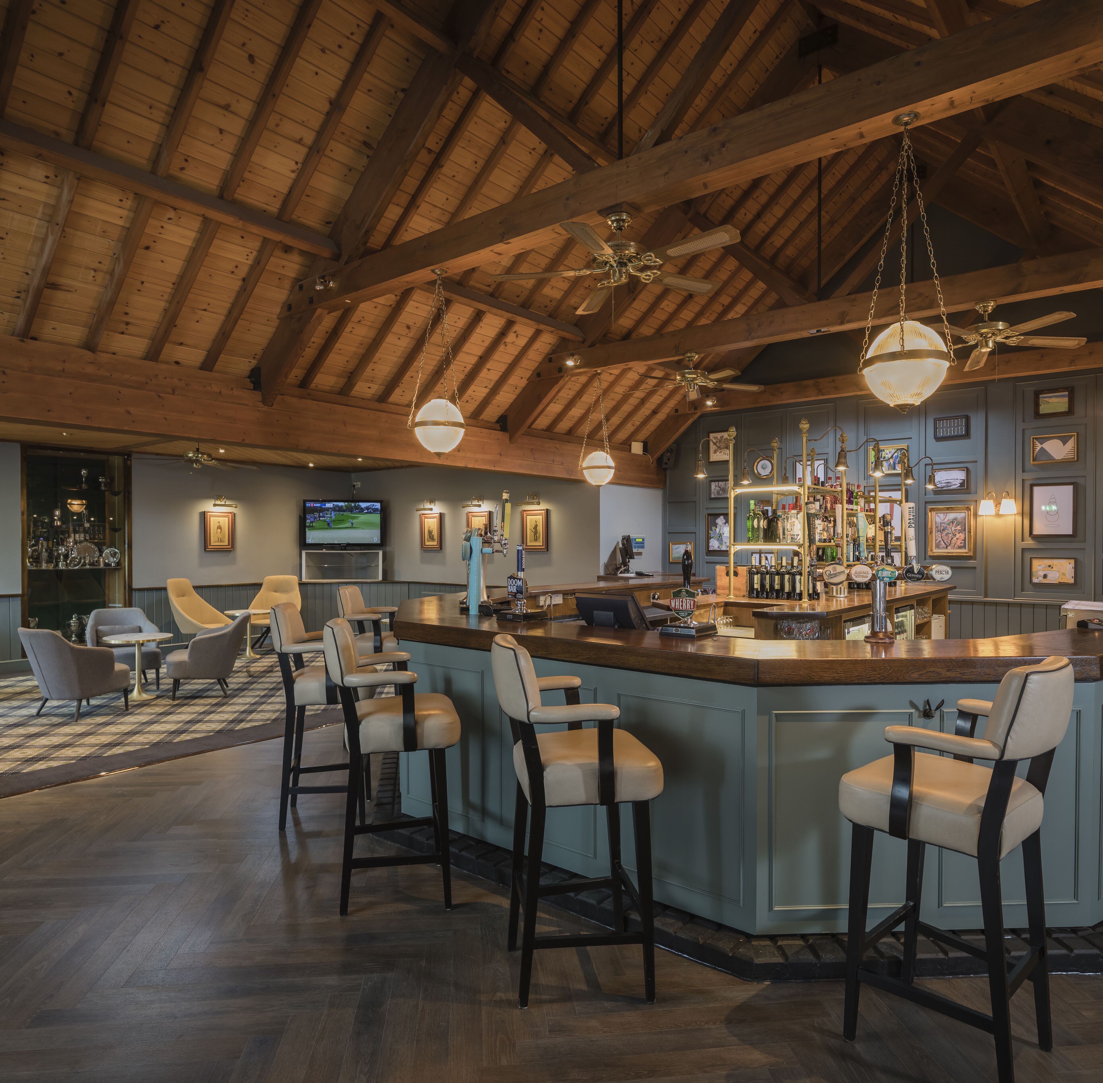 A bar area with wooden ceiling beams, bar stools, and a television screen.