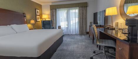 Una habitación de hotel con una cama grande, un escritorio con silla, un televisor, una lámpara de escritorio y un espejo.
