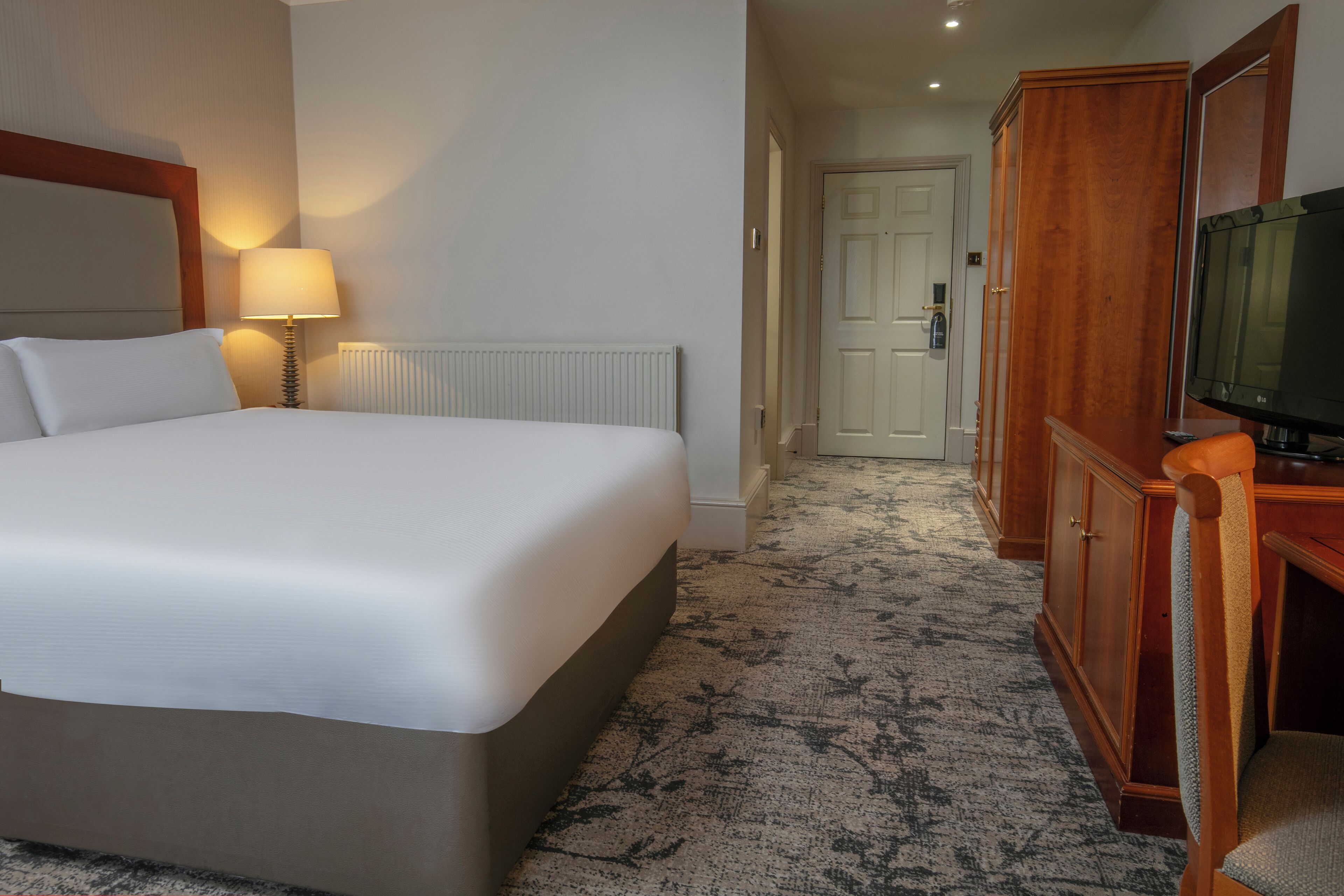 Une chambre d’hôtel avec un grand lit, une lampe de chevet, un téléviseur et une armoire en bois.