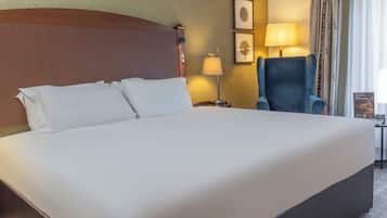 A large bed with white linens, a wooden headboard, a bedside lamp, and a blue armchair.