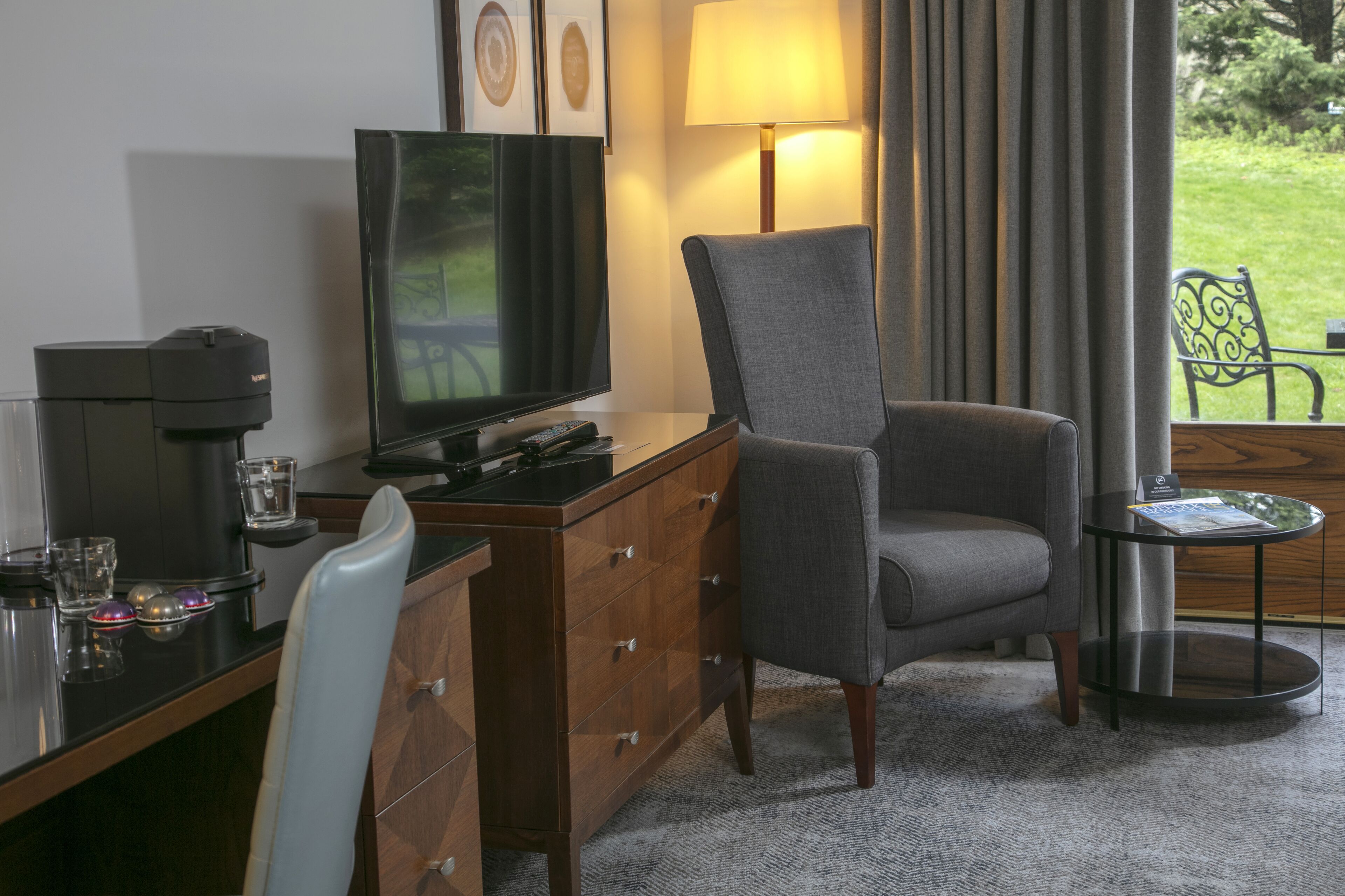 Habitación de hotel con escritorio, televisor, una silla, máquina de café y vistas al exterior.