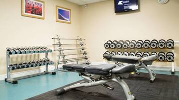 A gym with exercise equipment, a bench, dumbbells, and a wall clock.