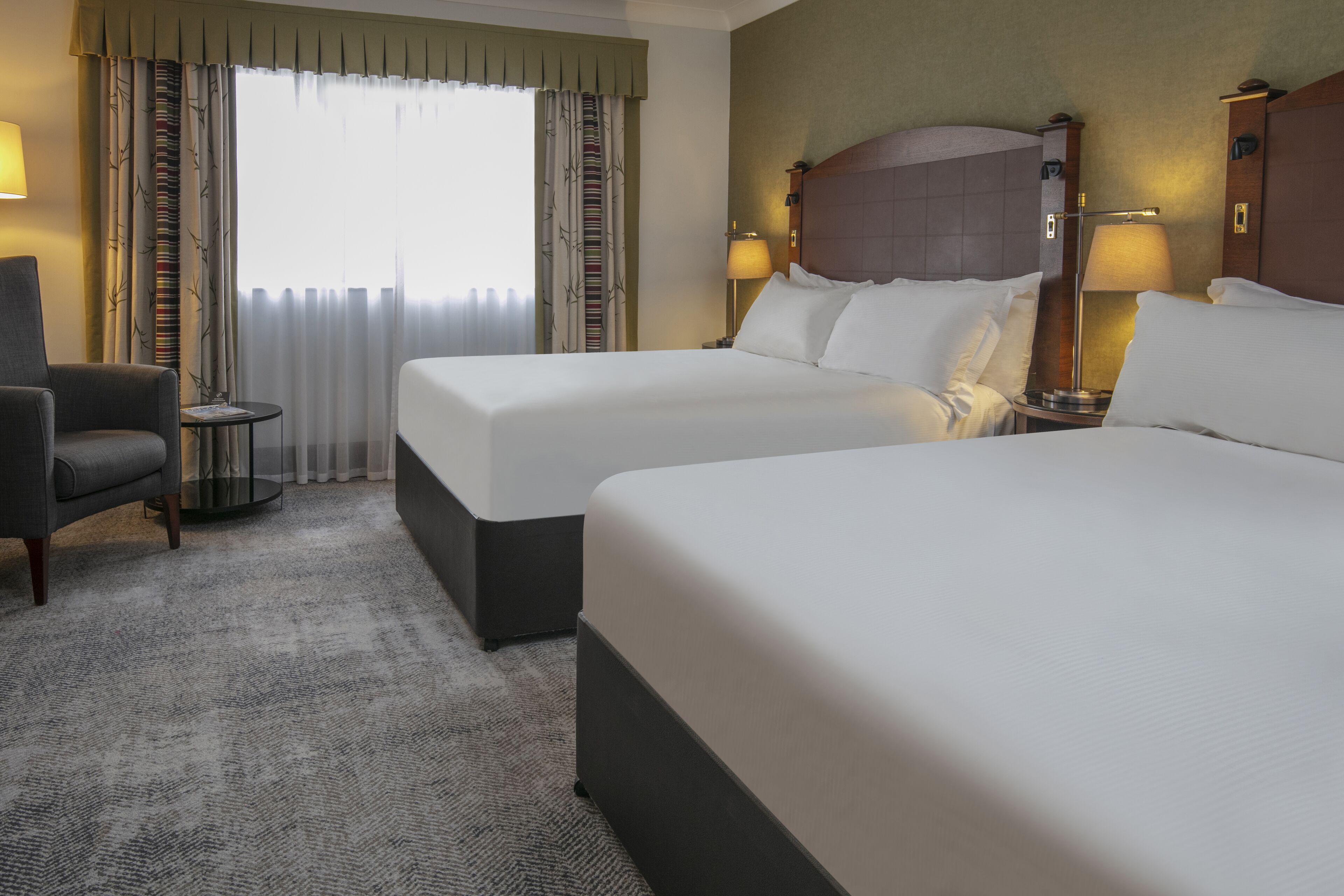 Una habitación de hotel con dos camas, una silla, una mesita y una lámpara.