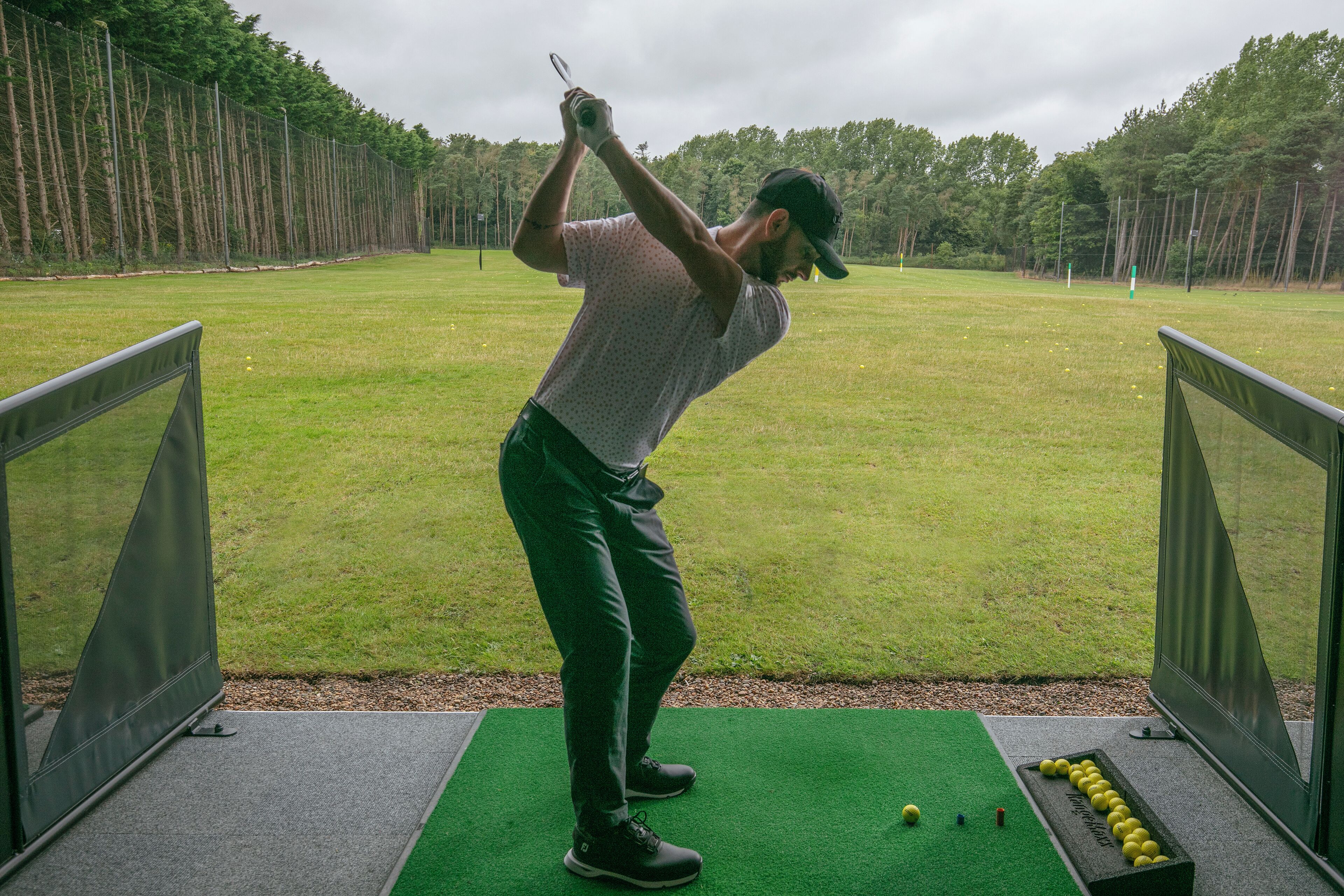 A golf course with a player in a white shirt and dark pants preparing to swing.